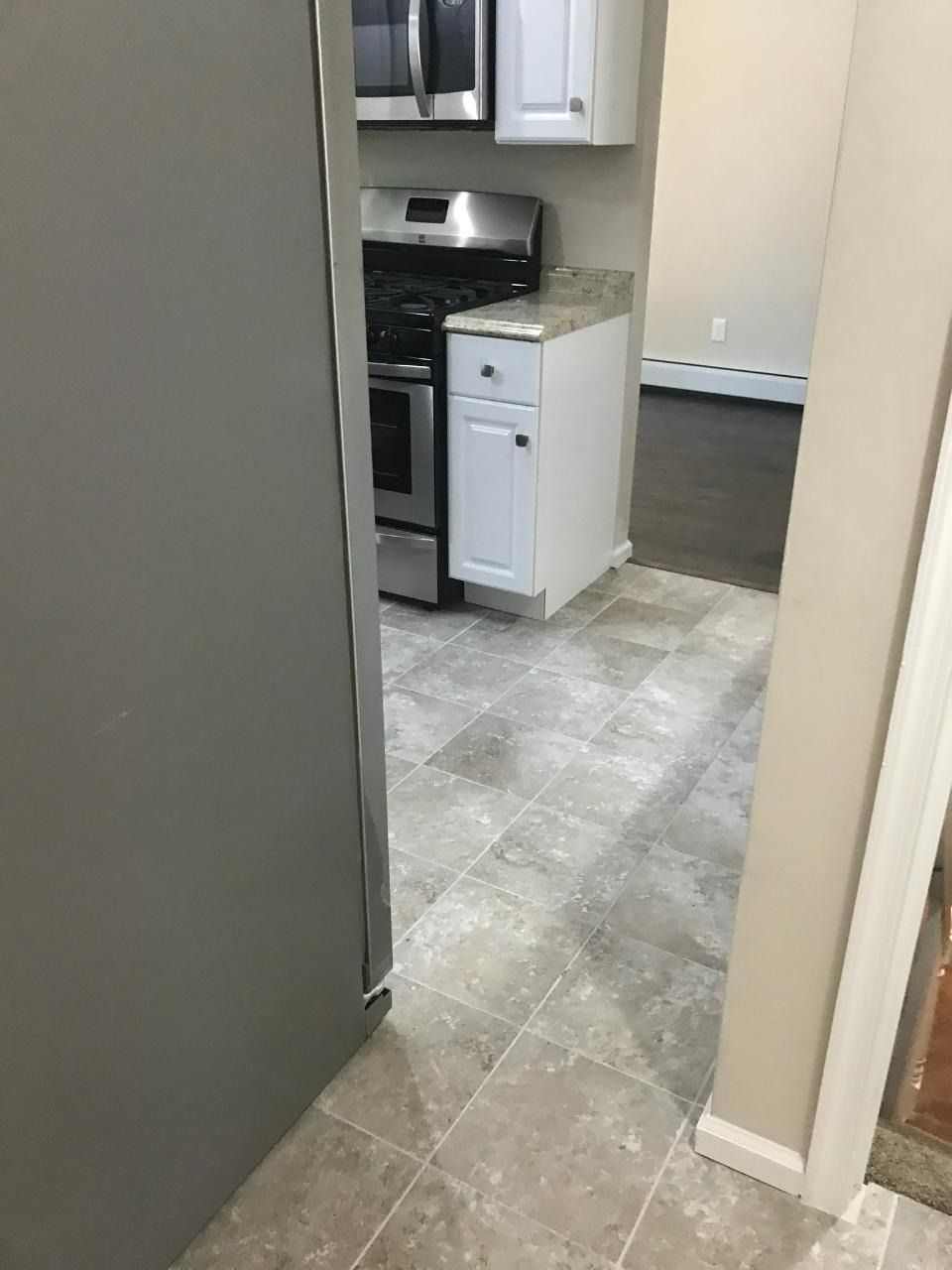 Kitchen interior with gray flooring, white cabinets, stainless steel appliances, and a refrigerator.