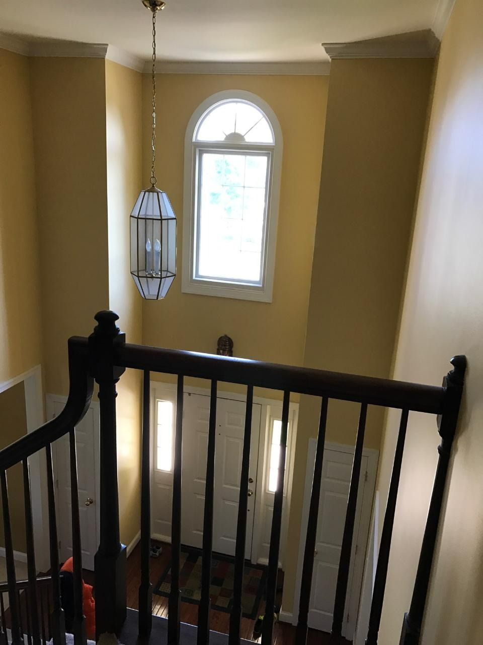 Staircase view, front door visible, topped by an arched window, with a hanging light fixture. Yellow walls.