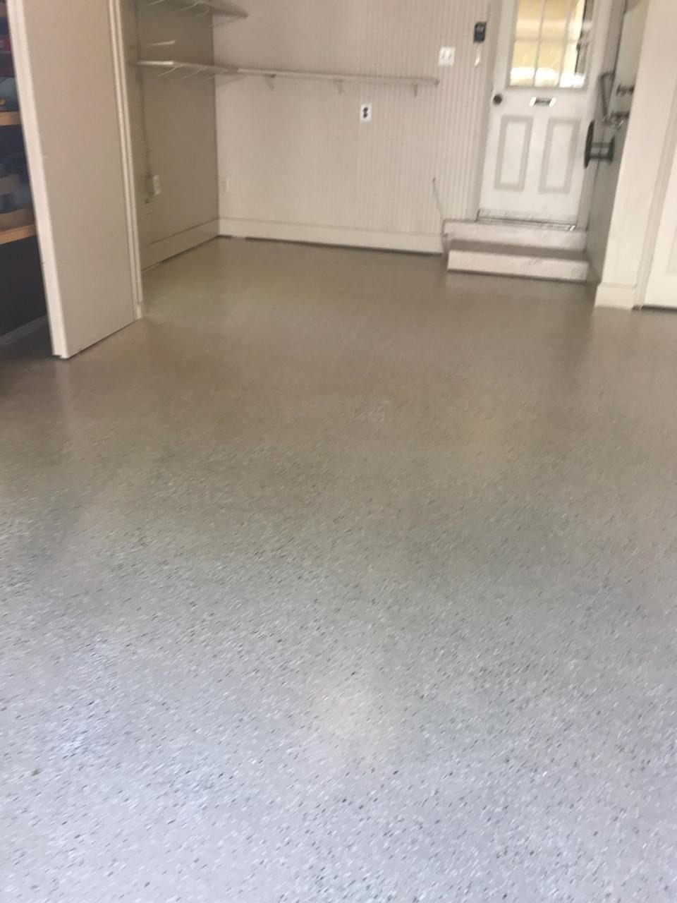 Garage interior with a speckled, gray epoxy floor, white walls, a door, and a shelving unit.