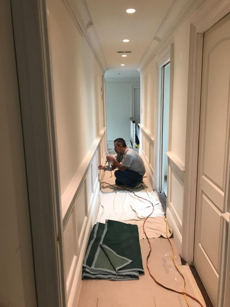Person working on electrical wiring in a hallway with white trim and recessed lighting.