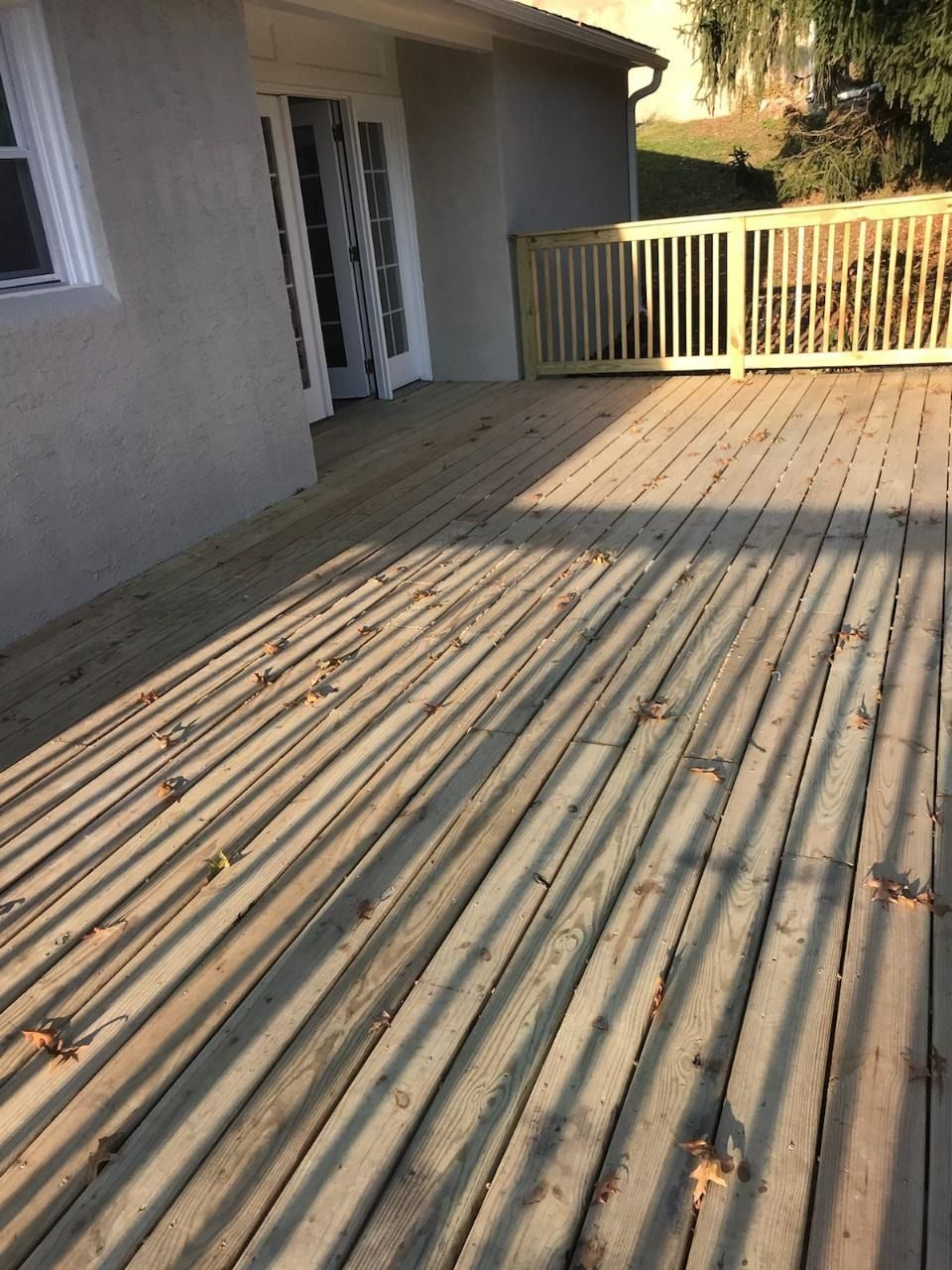 Wooden deck with shadows, leading to a house with glass doors and a white fence.