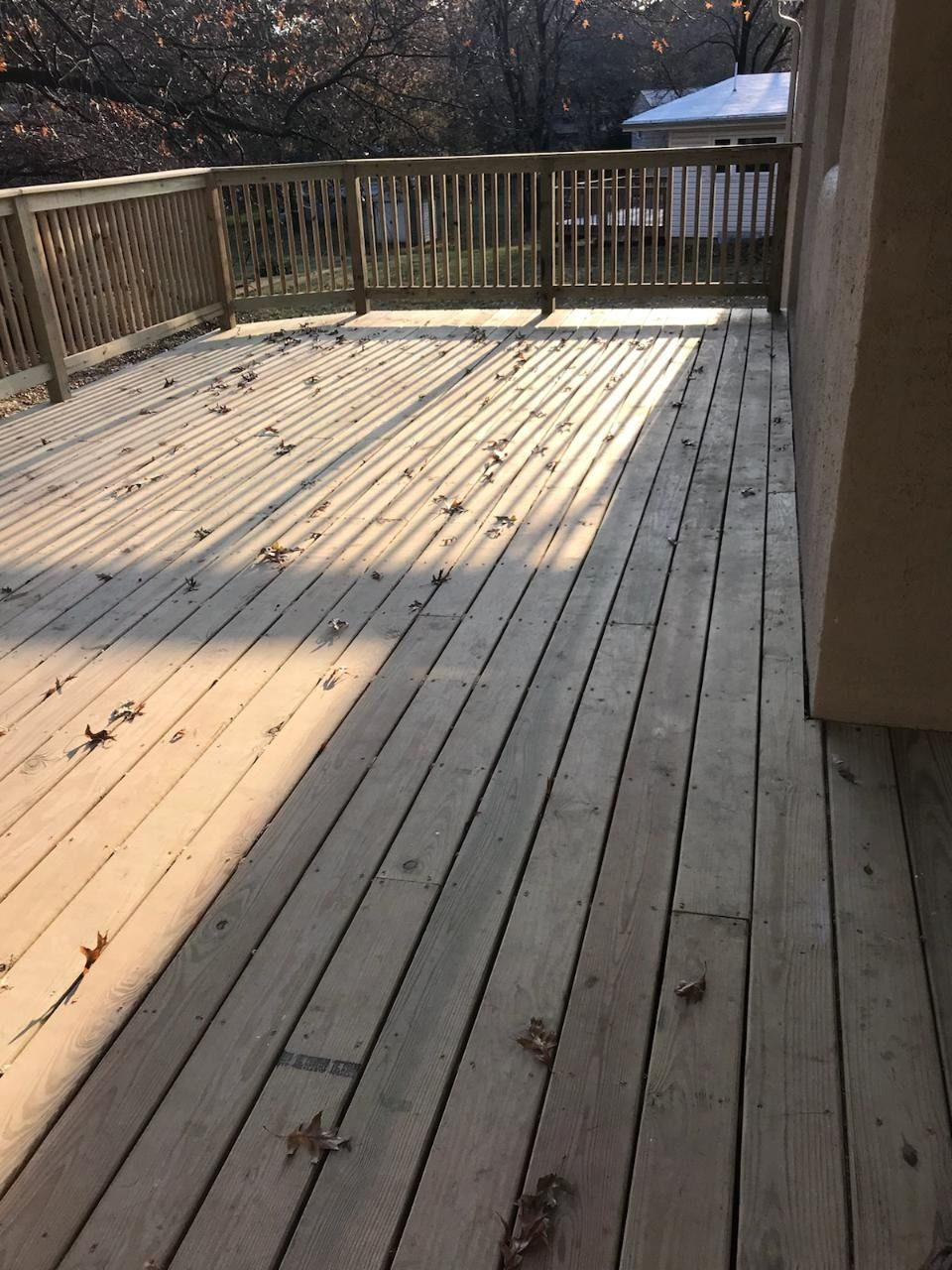 Wooden deck with railing, covered in fallen leaves.