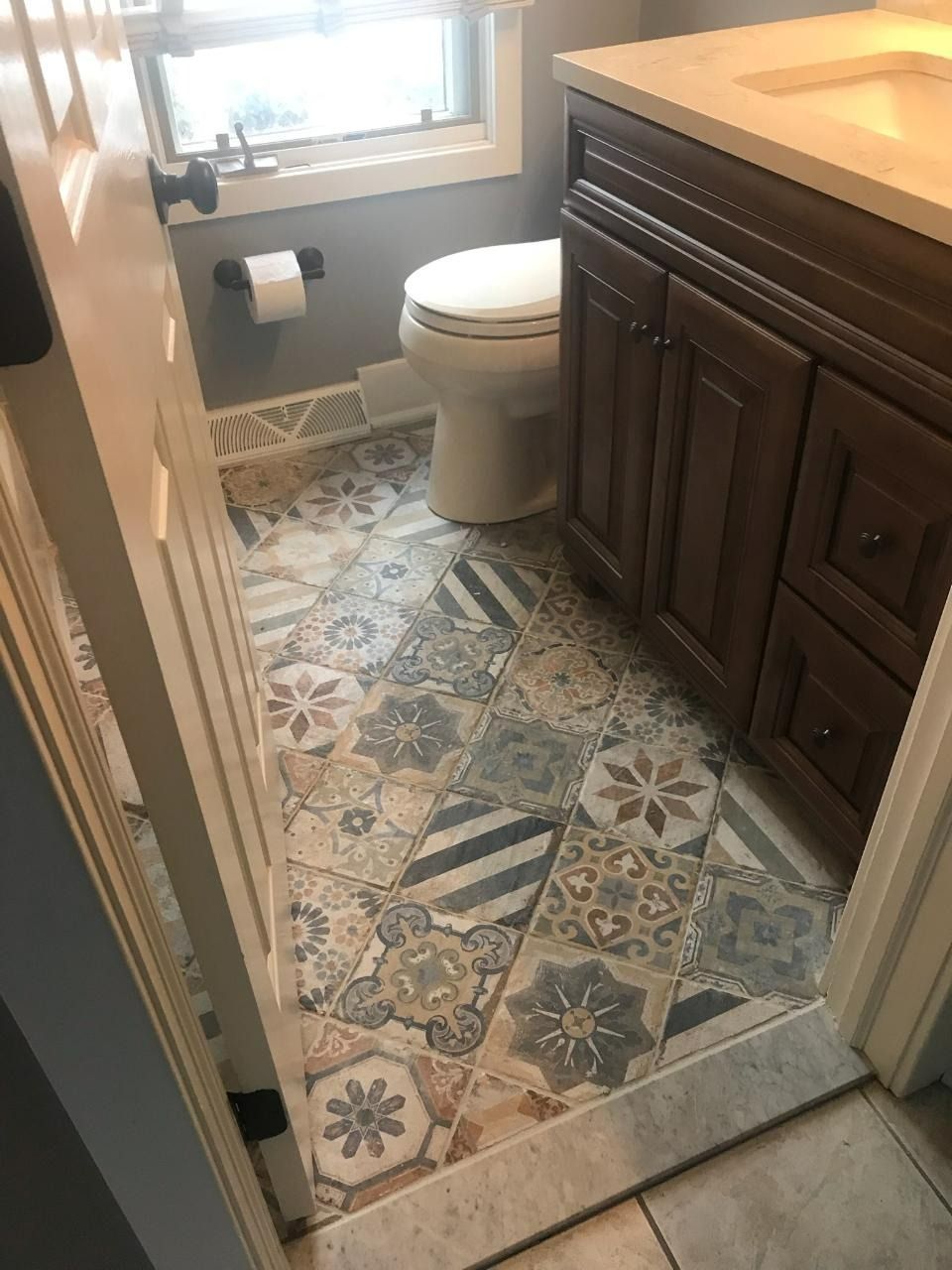 Bathroom with patterned floor tiles, toilet, dark wood vanity, and small window.