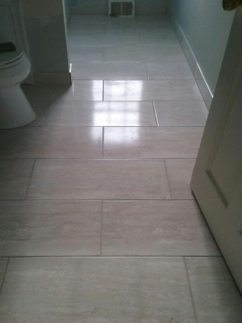 Bathroom floor tiled with light gray rectangular tiles, partially showing toilet and door.