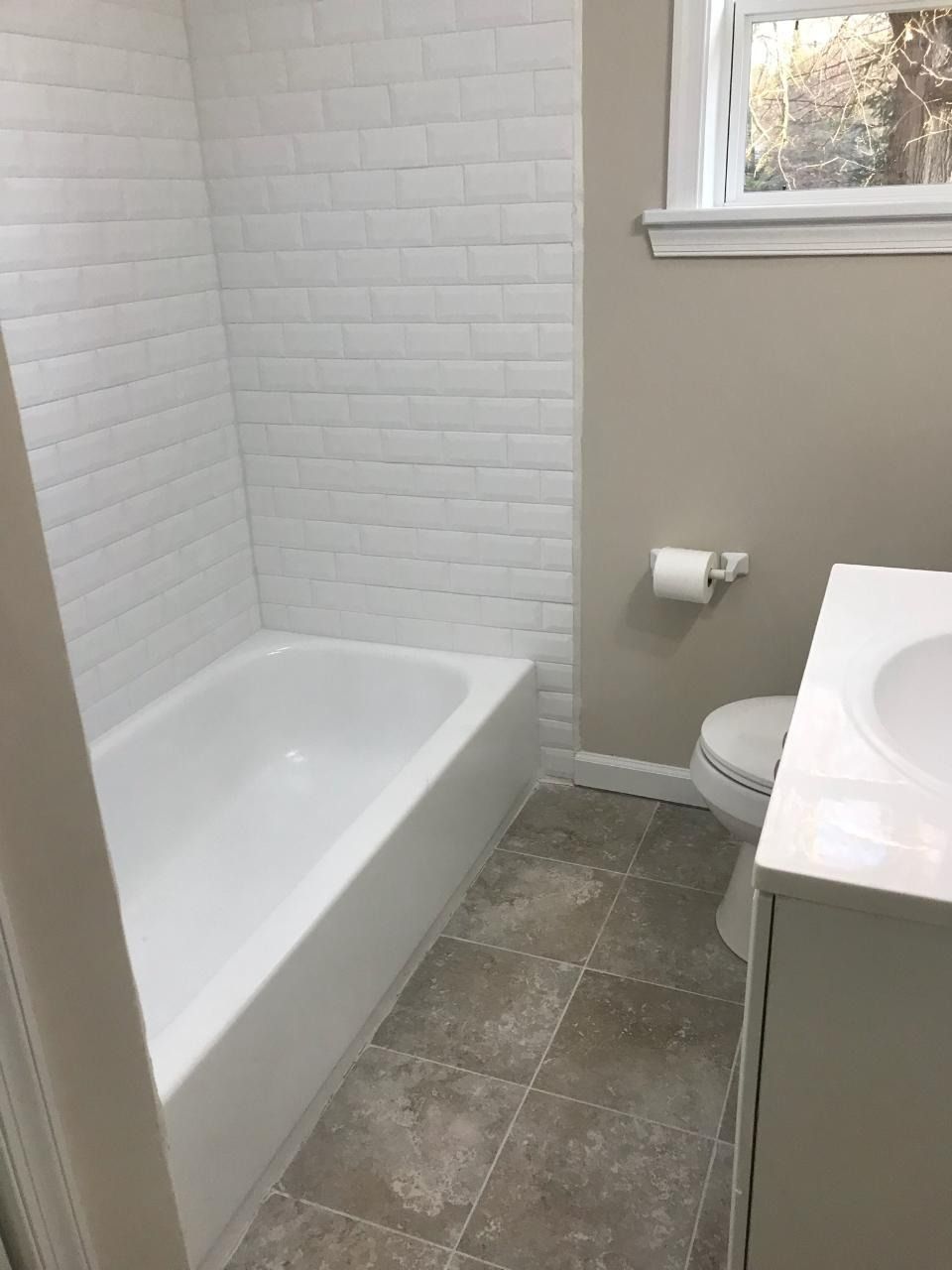 Bathroom with white tub, subway tile, beige walls, gray floor, and toilet.