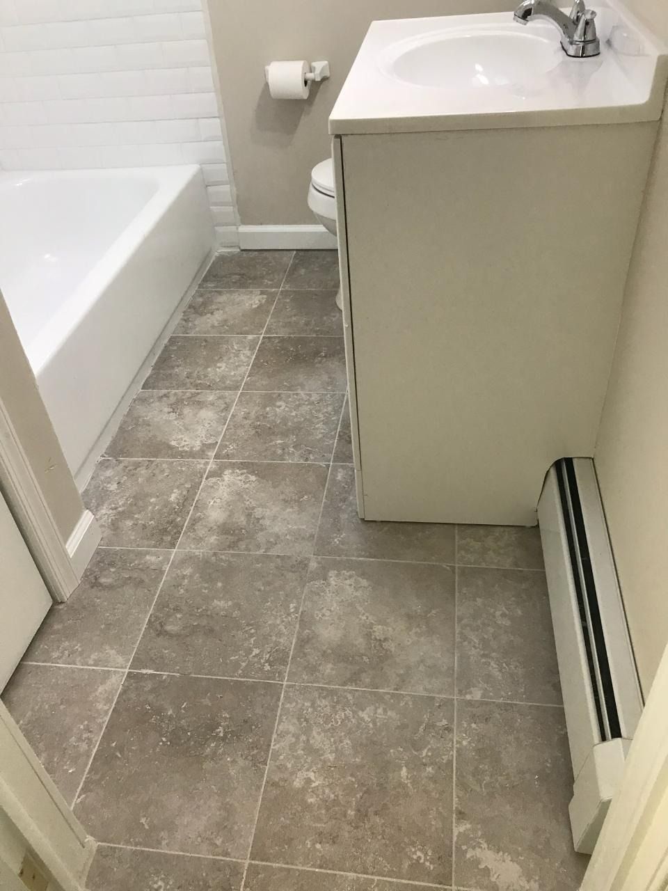 Bathroom with white tub, sink, and tile floor. A radiator is visible.