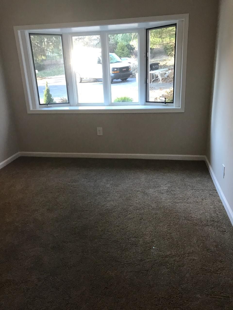Empty room with beige walls, brown carpet, and a large window.