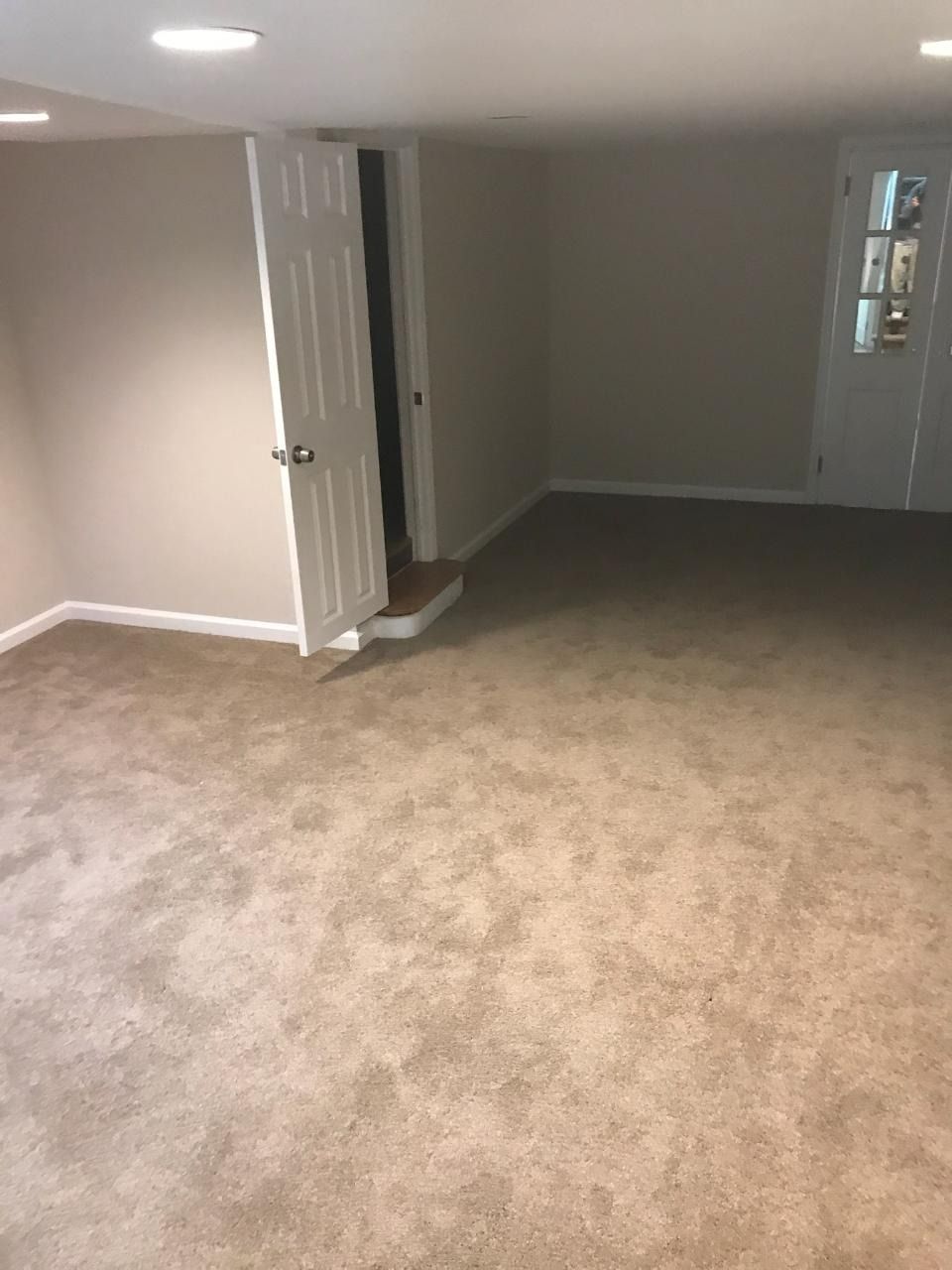 A room with beige carpet, light-colored walls, and a door leading to a slightly elevated area.