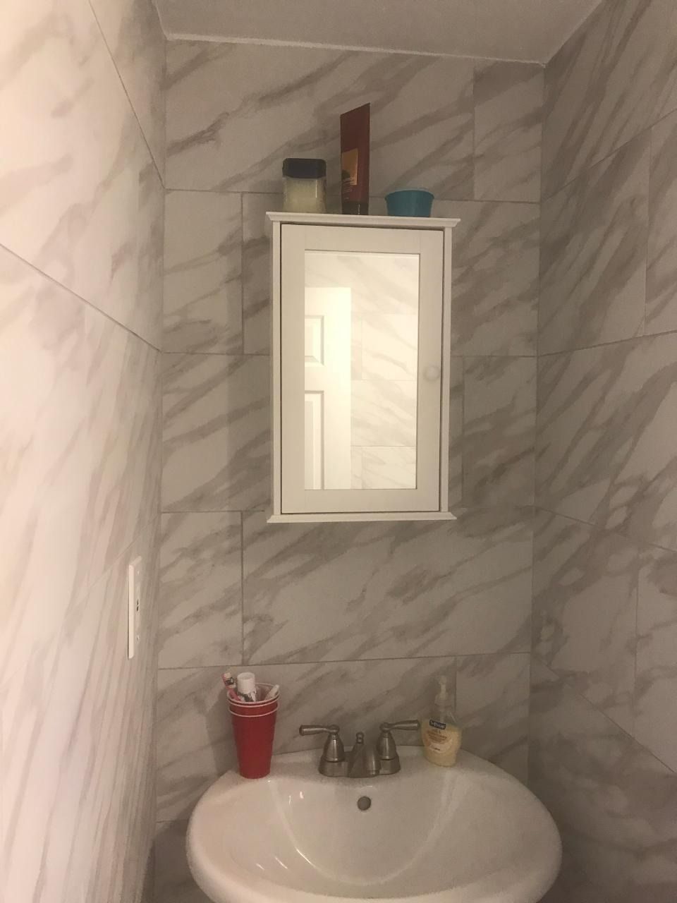 Bathroom with white sink, medicine cabinet, and marble-patterned wall tiles. Toothbrush holder and soap dispenser visible.