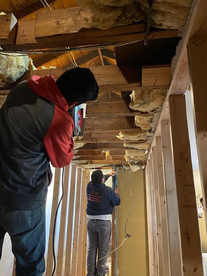 Two workers remodel an attic, cutting wood with power tools.