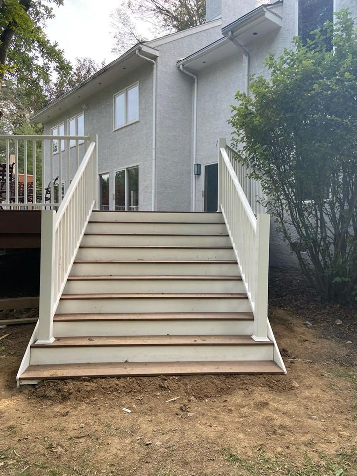 Exterior view: a staircase with white railings leading to a house with light gray siding and wooden stairs.