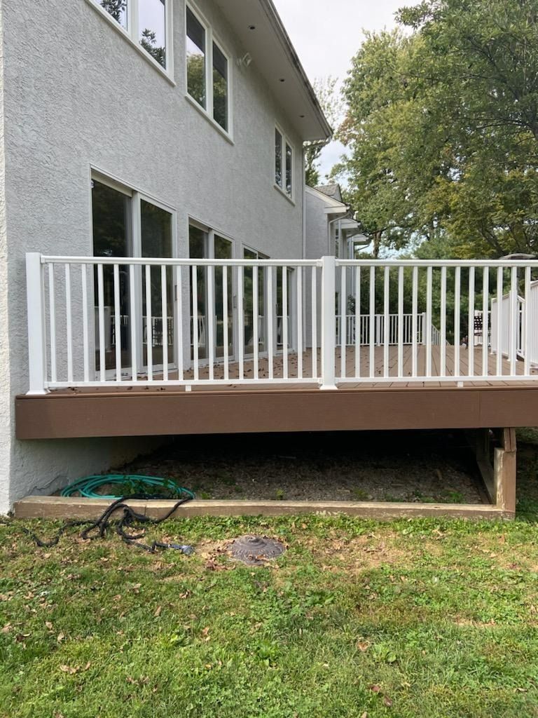 White-railed deck attached to a light gray house with tall windows, set on green grass.