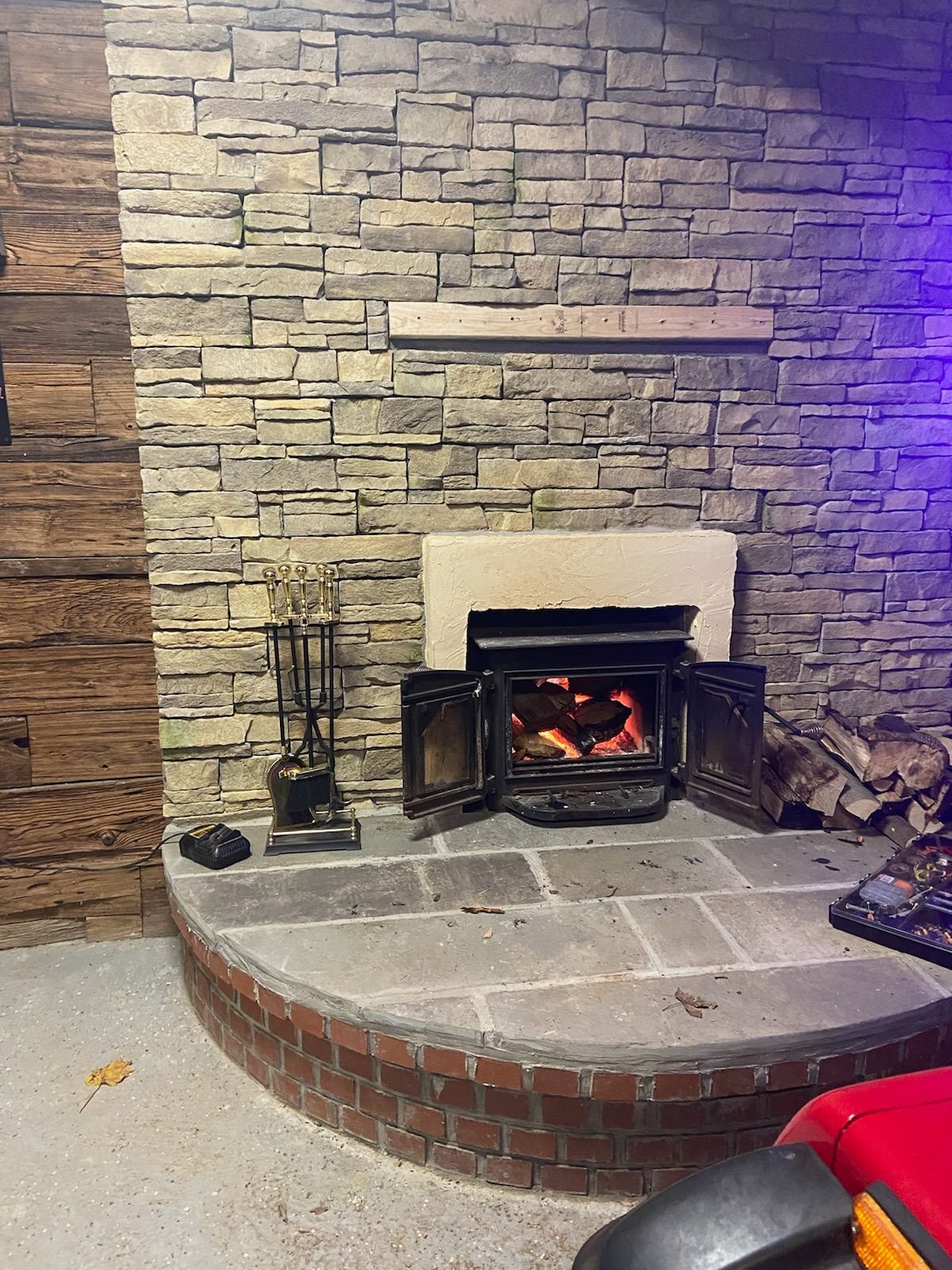 Fireplace with lit fire, on stone hearth and brick base, in a stone-walled interior.