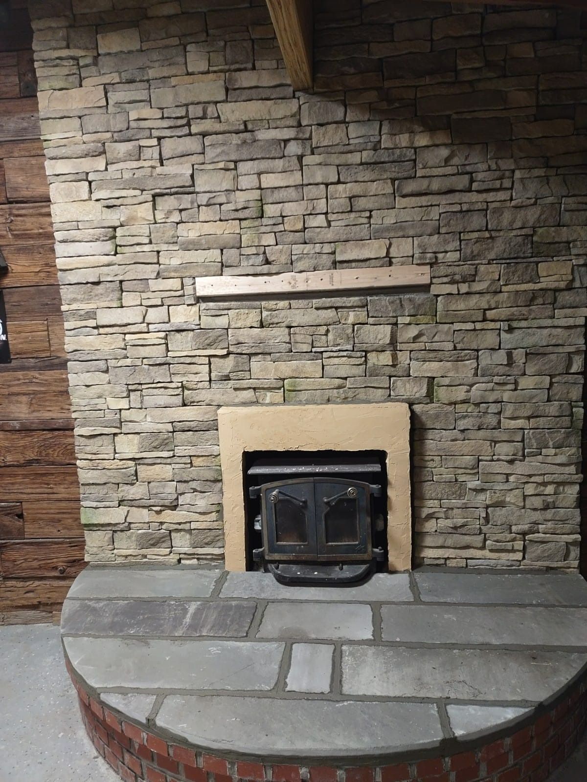 Fireplace with stone surround, wood mantel, and hearth. A stove is inside. Brick base.