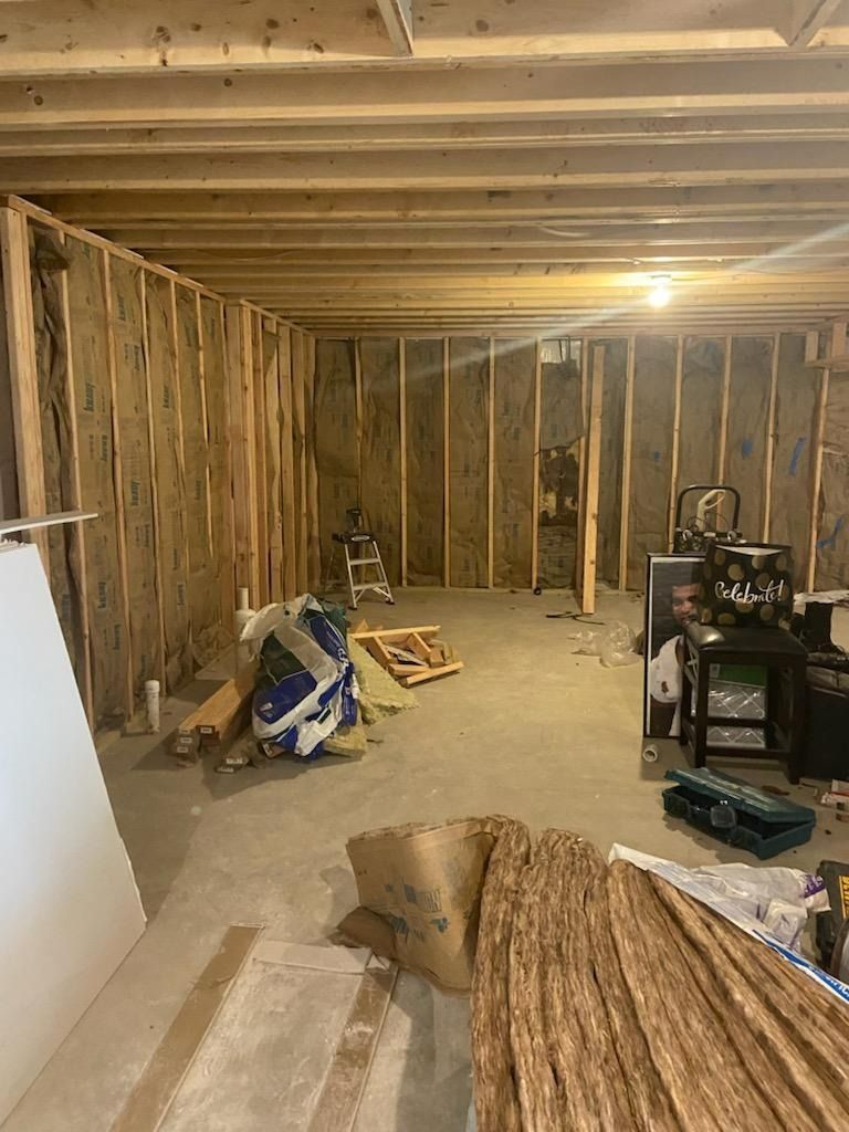 Basement under construction. Wood framing, insulation, concrete floor, and scattered materials.