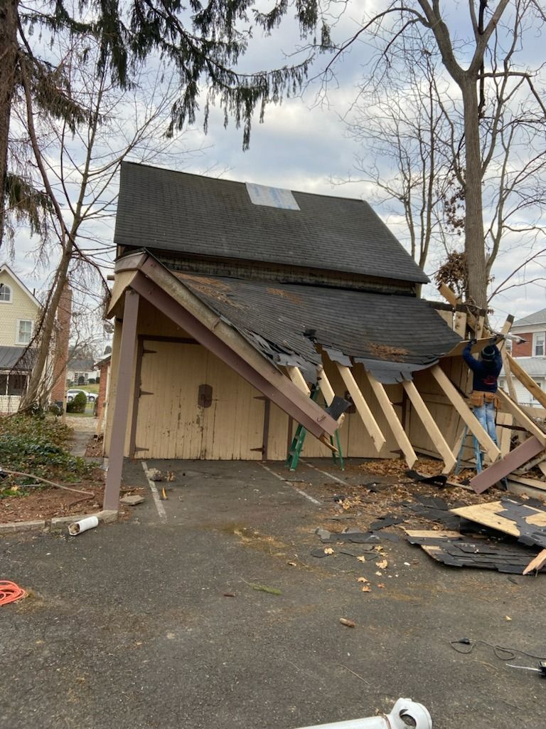 Garage being demolished; roof partially collapsed; workers on scaffolding; beige building.