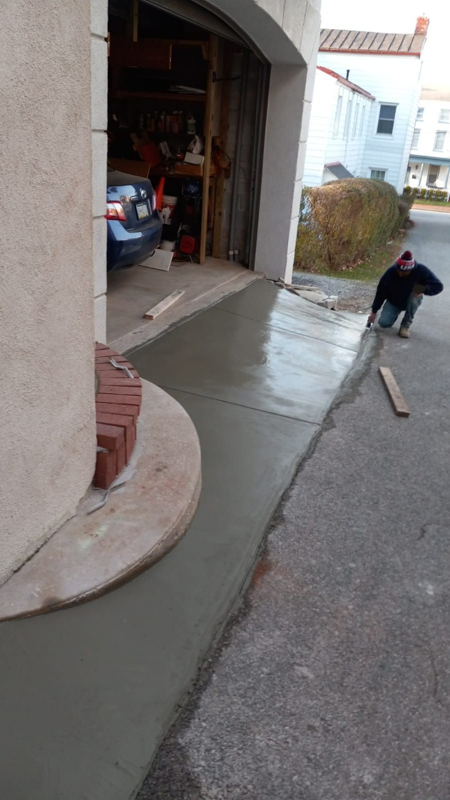 Person leveling wet cement driveway with garage in the background.