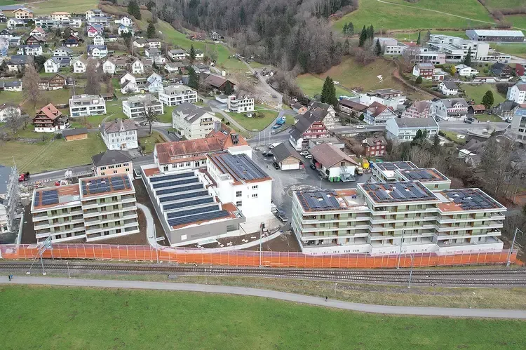 Luftaufnahme von modernen Wohnhäusern mit Solaranlagen, neben einer Eisenbahnlinie und einer kleinen Stadt.