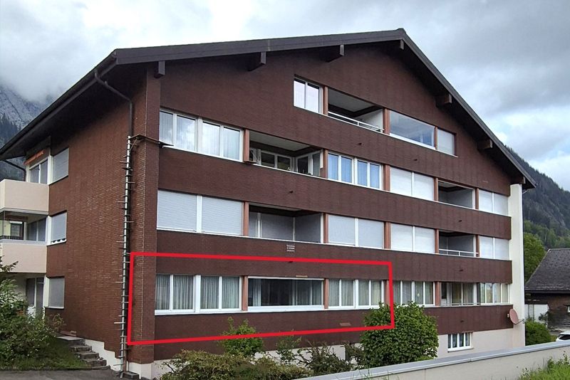 Ein vierstöckiges, braunes Backsteingebäude mit Satteldach, dessen Fenster im Erdgeschoss von einem roten Kasten eingefasst sind.