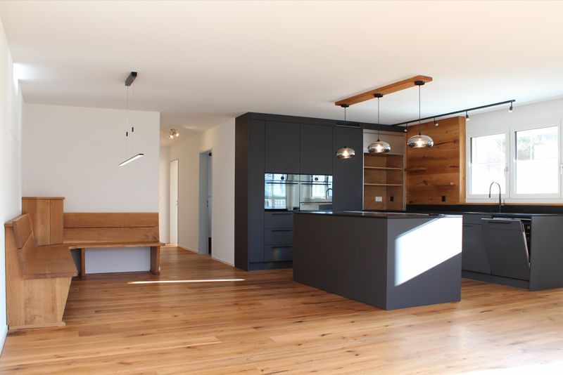 Moderne Küche mit schwarzer Kochinsel, passenden Schränken und Holzboden mit eingebauter Eckbank.