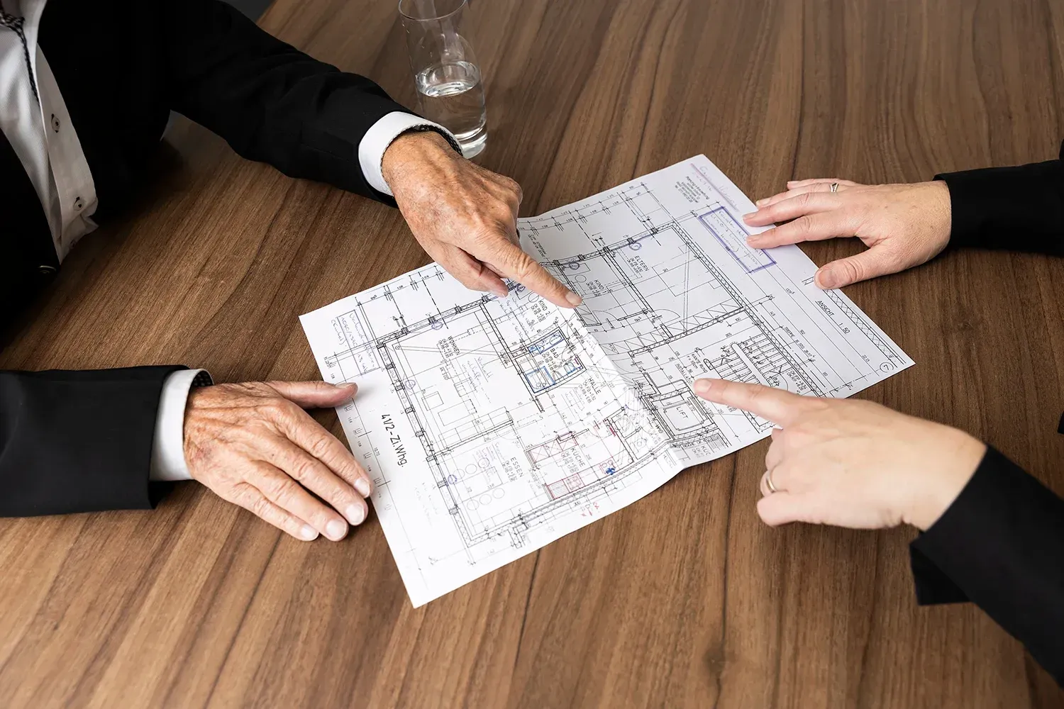 Zwei Personen in Geschäftskleidung betrachten gemeinsam einen Grundriss an einem Holzschreibtisch.