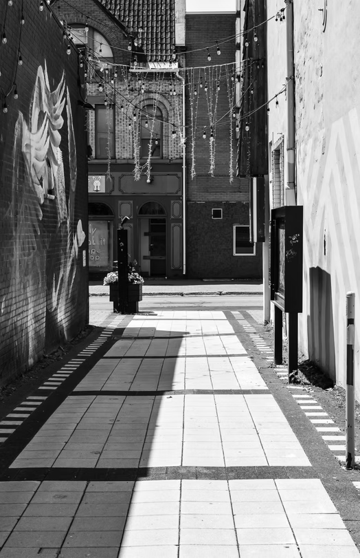 Narrow sunlit alley with brick walls and tiled pavement in black and white