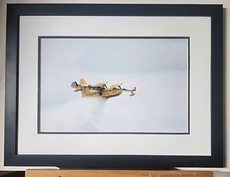 Framed photo of a yellow propeller plane flying against a pale sky