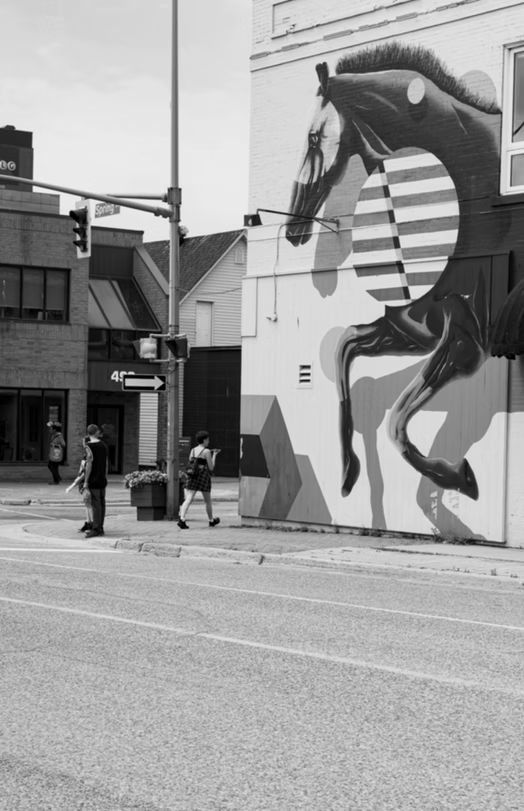 Black-and-white street scene with a large horse mural on a building and two people walking nearby.