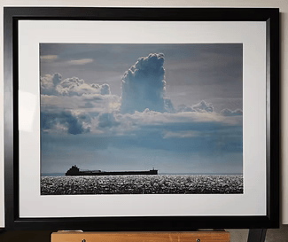 Framed seascape photo of a cloudy sky over a calm ocean with a ship silhouette near the horizon