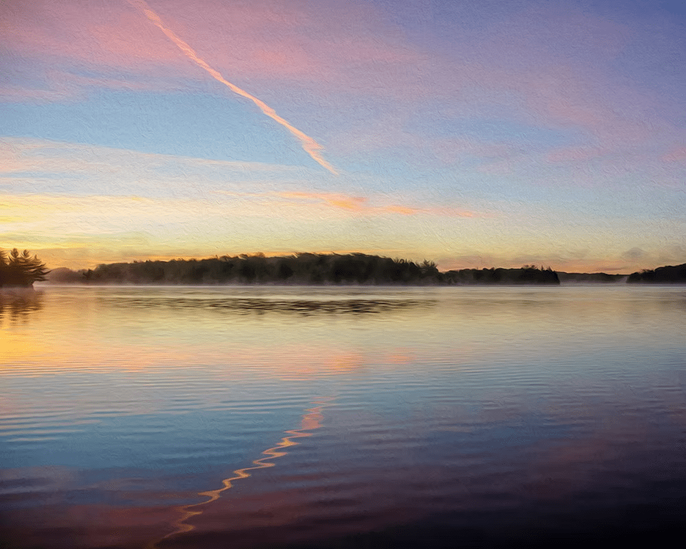 Calm lake at sunrise with pink-orange sky and a diagonal contrail reflecting on the water