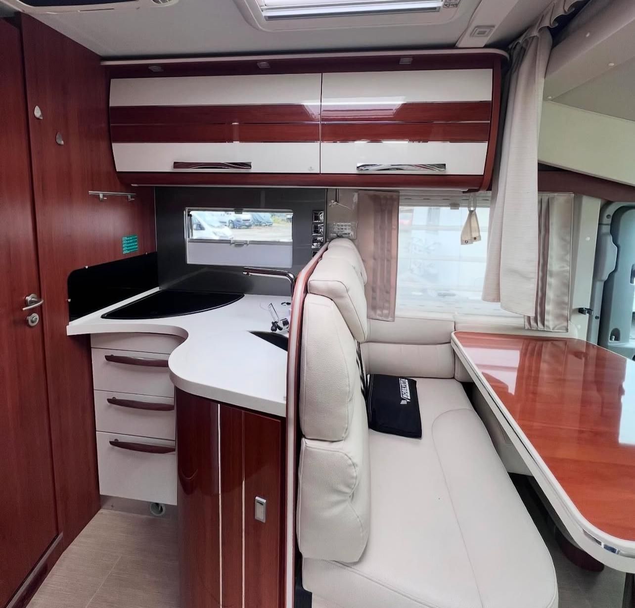 Interno di un moderno camper con cucina, zona pranzo e pensili.