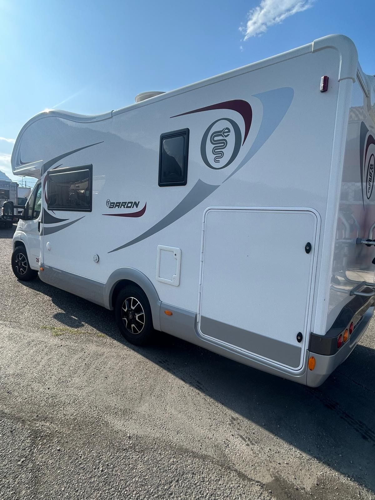 Veicolo ricreativo bianco e grigio con ruote nere parcheggiato sull'asfalto.