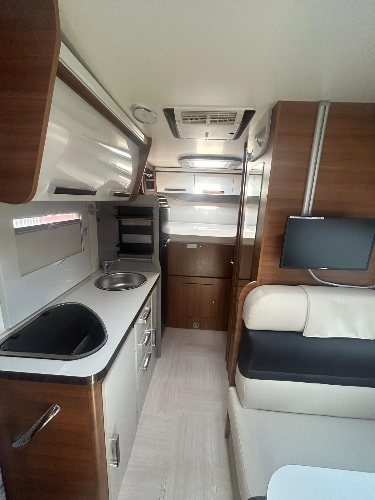 Vista interna di un camper con cucina, area salotto e TV montata.