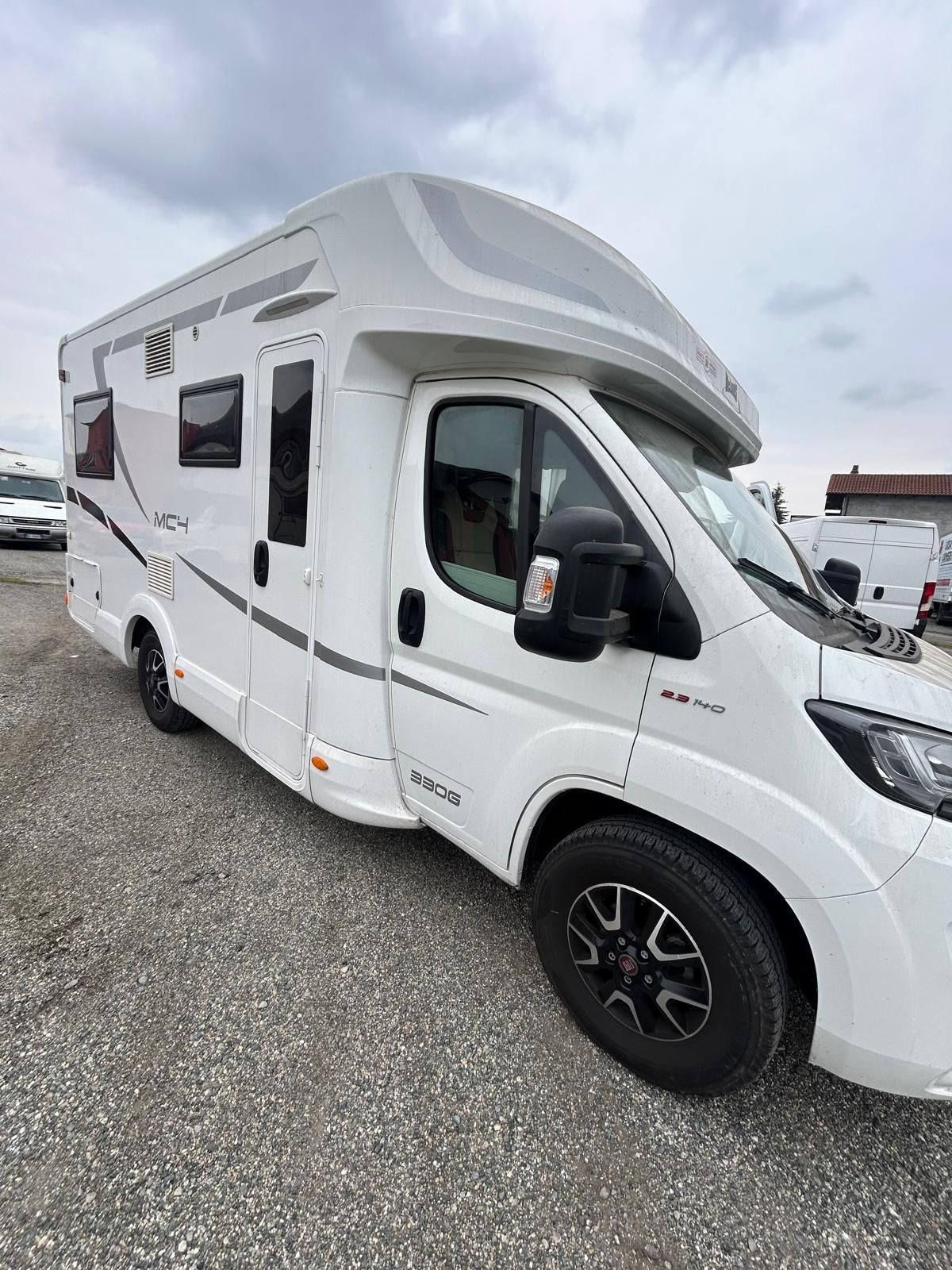 Camper bianco parcheggiato sulla ghiaia, cielo nuvoloso sopra di noi.