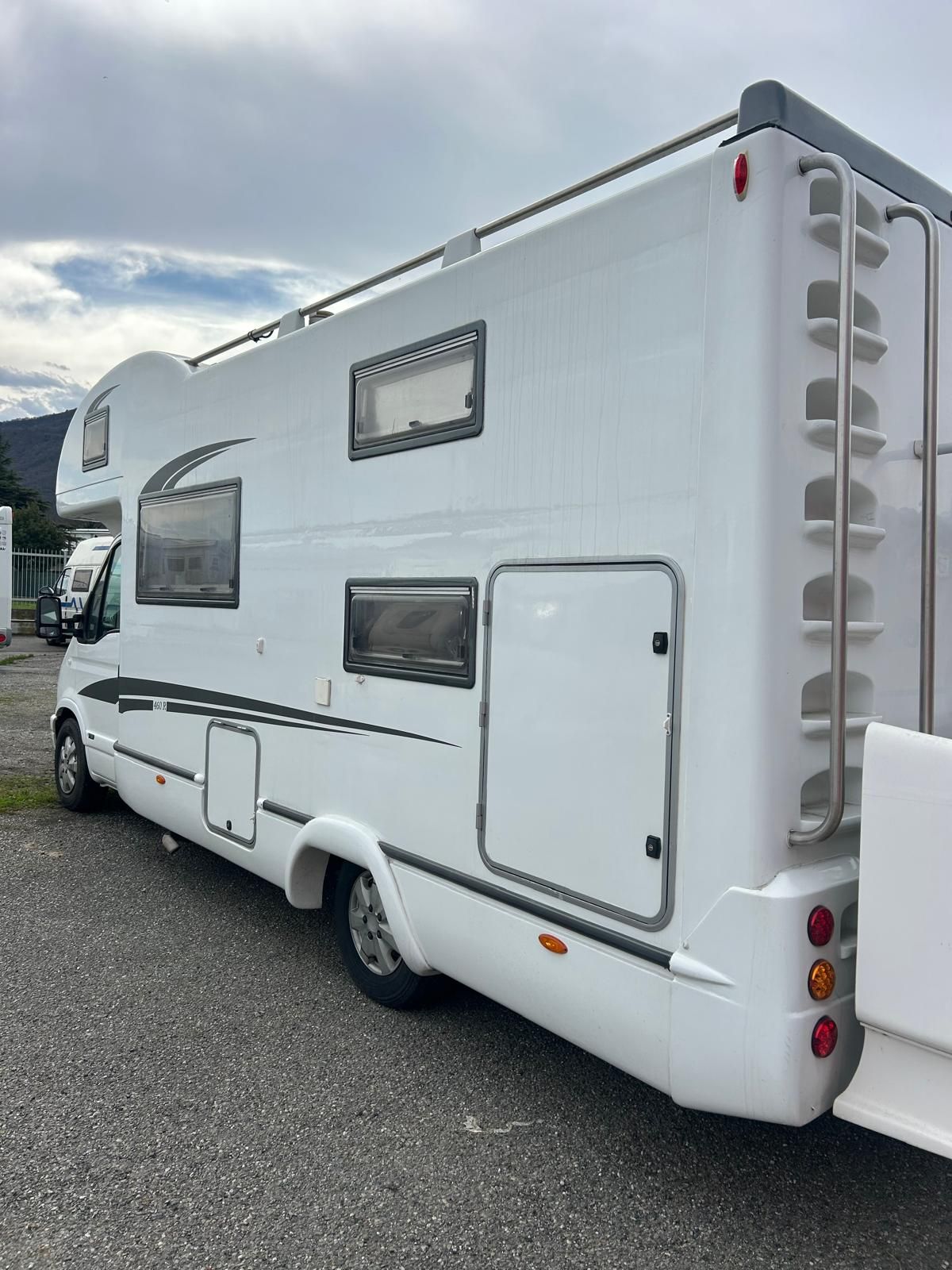 Veicolo ricreativo bianco parcheggiato sulla ghiaia, con una scala sul retro.