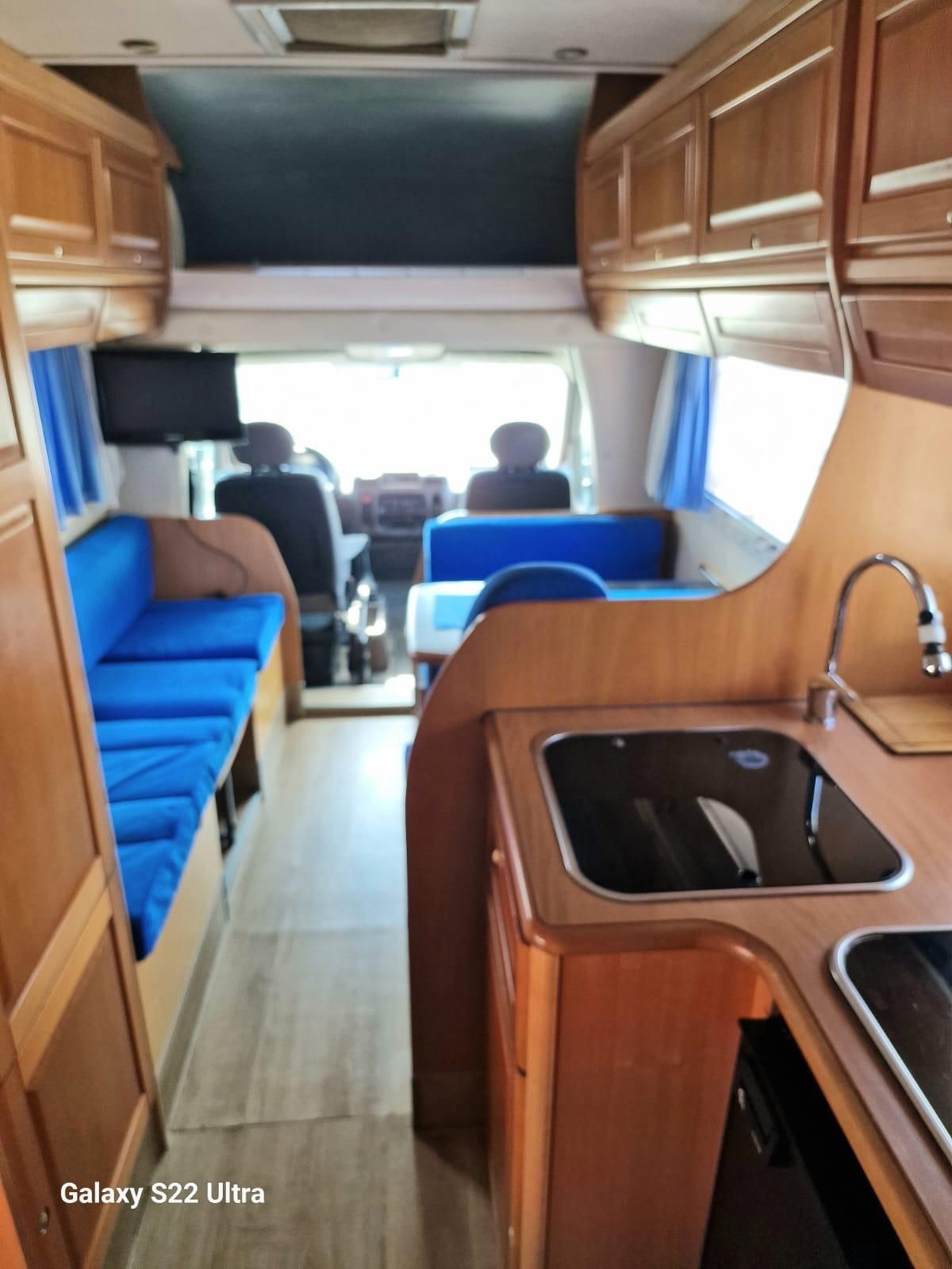 Interno di un camper con cuscini blu, mobili in legno e zona cucina.