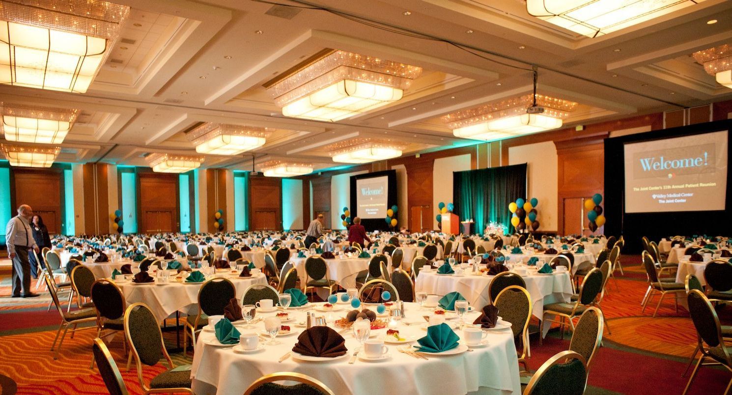 Large banquet hall set up with round tables, teal napkins, and stage with welcome message.