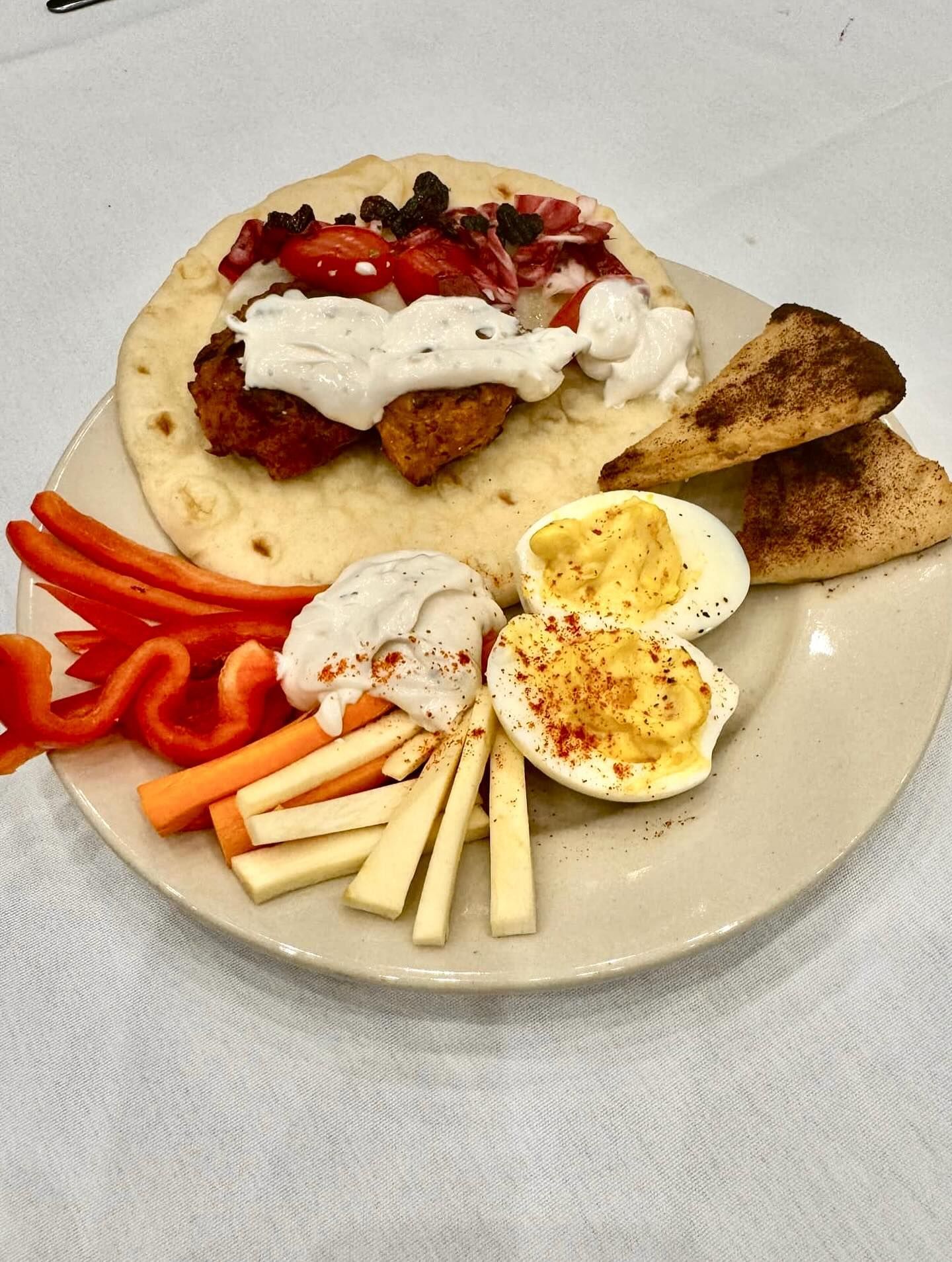 A plate featuring a chicken gyro on pita bread, hard-boiled eggs, pepper strips.