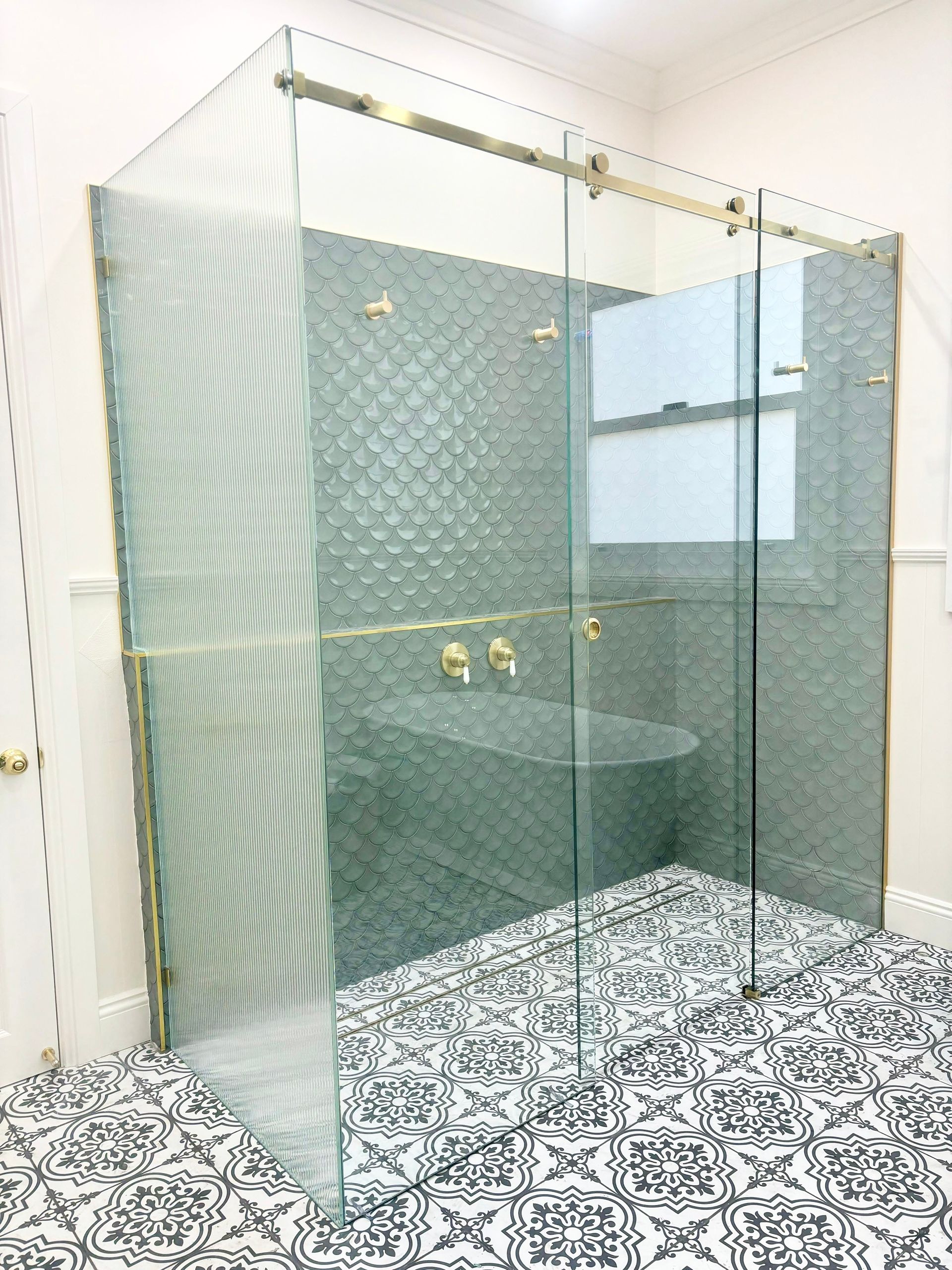modern frameless glass shower screen with gold fittings and patterned floor tiles