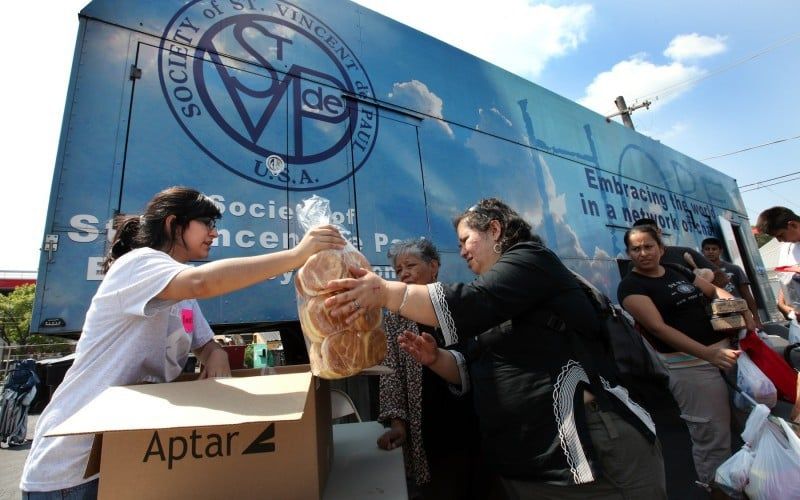 People receiving food from a Society of St. Vincent de Paul truck. A volunteer hands a loaf of bread to a woman.