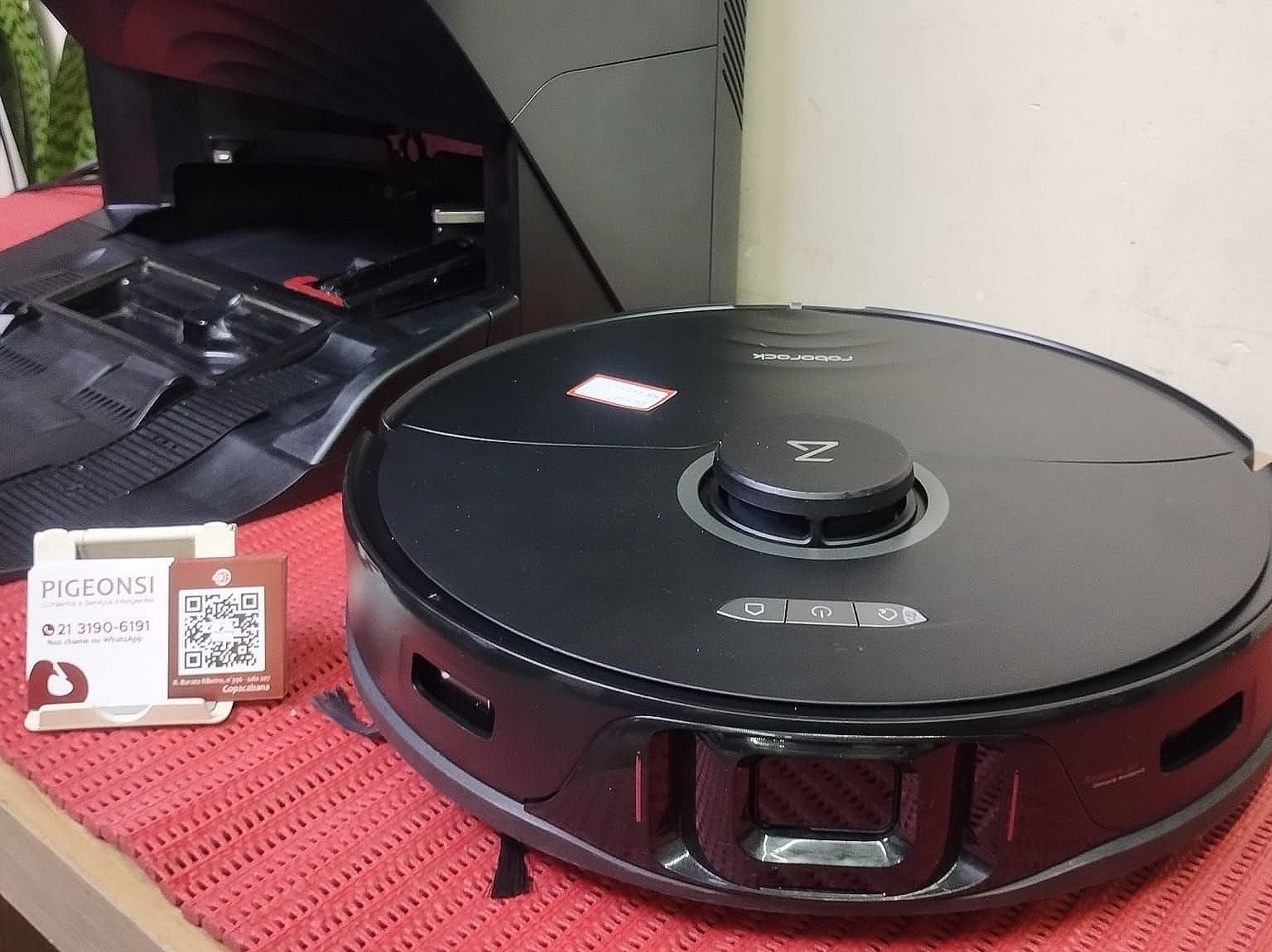 Um aspirador de pó robótico preto está sobre uma toalha de mesa vermelha