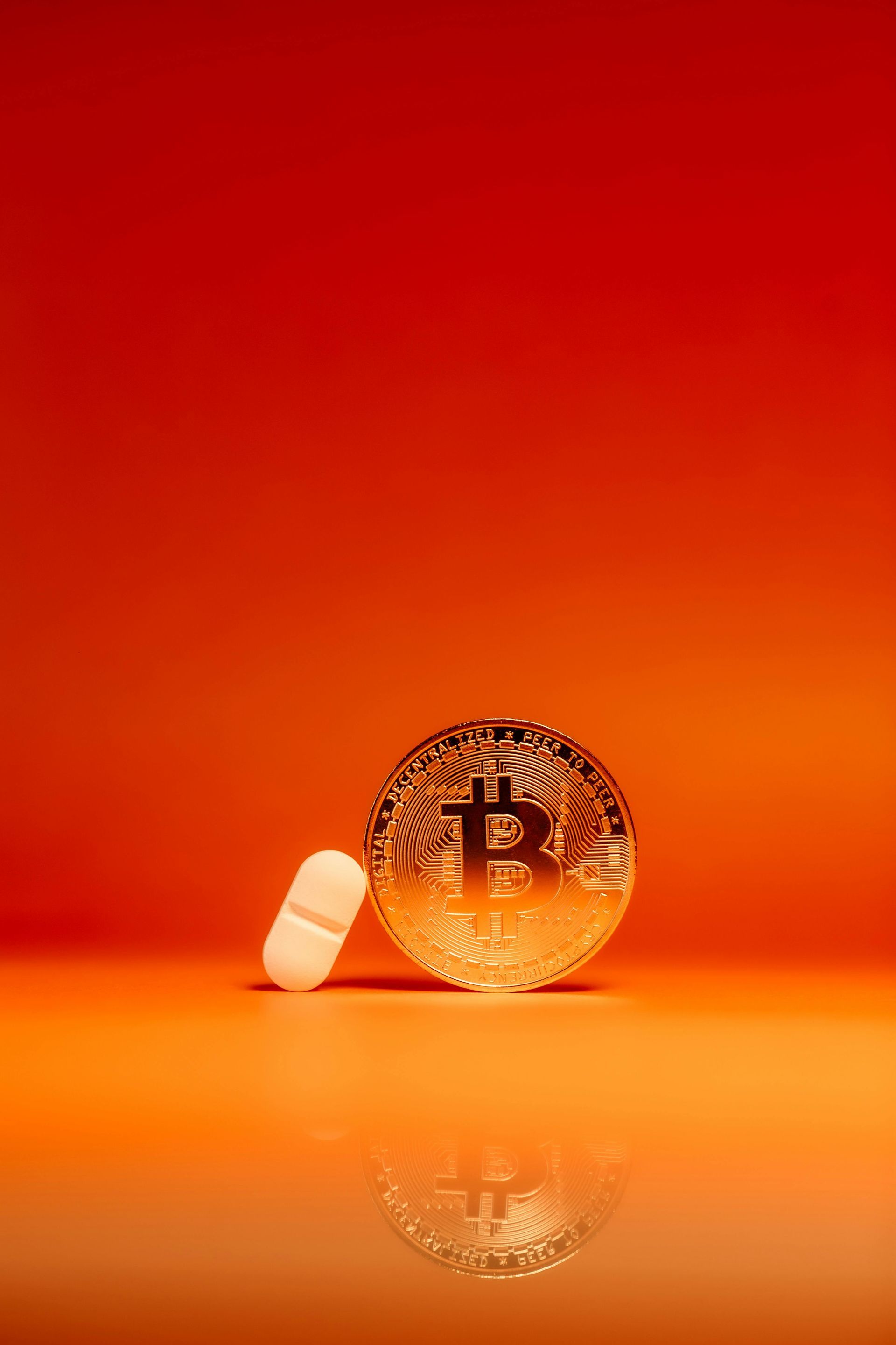 Um bitcoin e uma pílula em um fundo laranja.