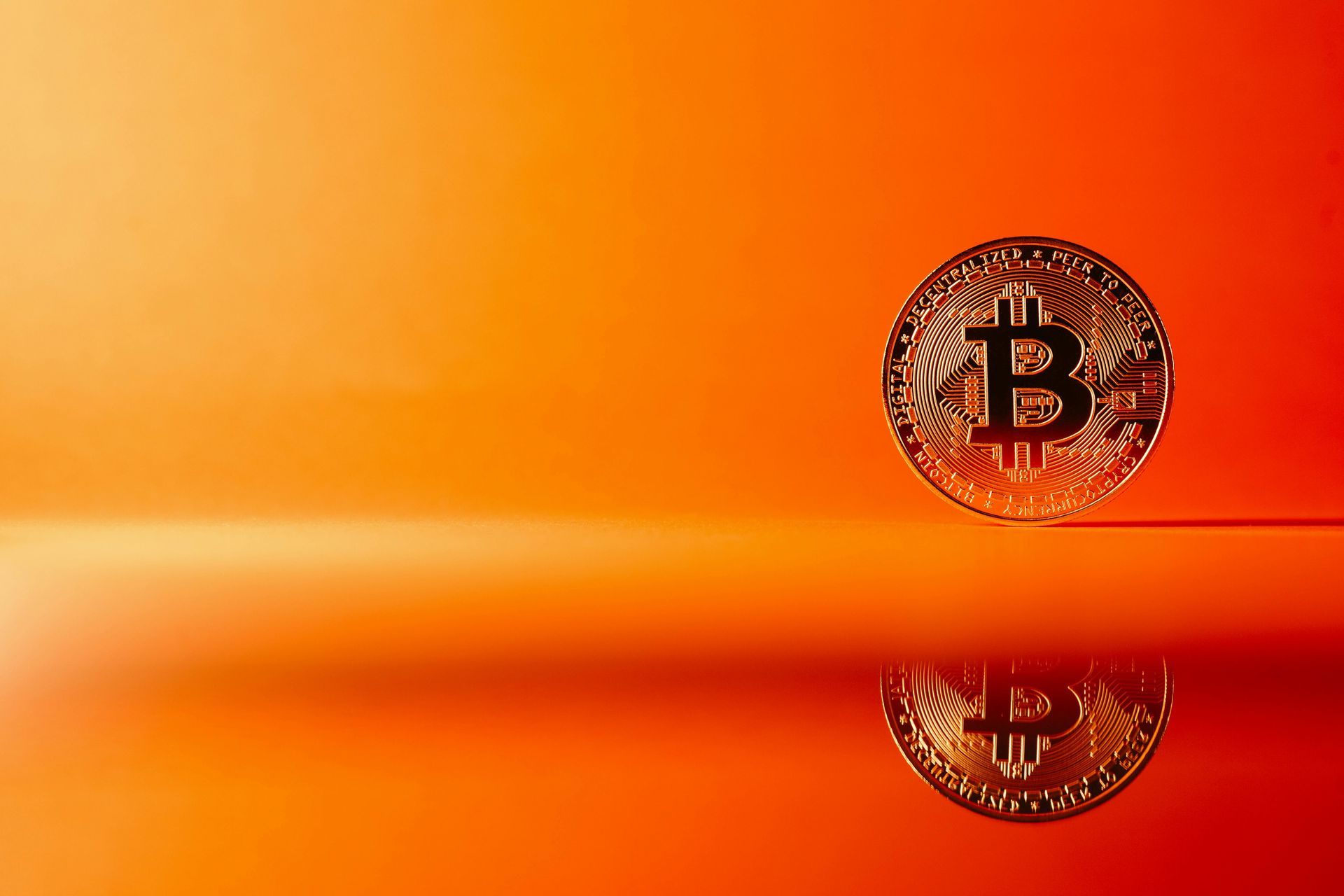 Uma moeda bitcoin está sobre uma superfície vermelha.