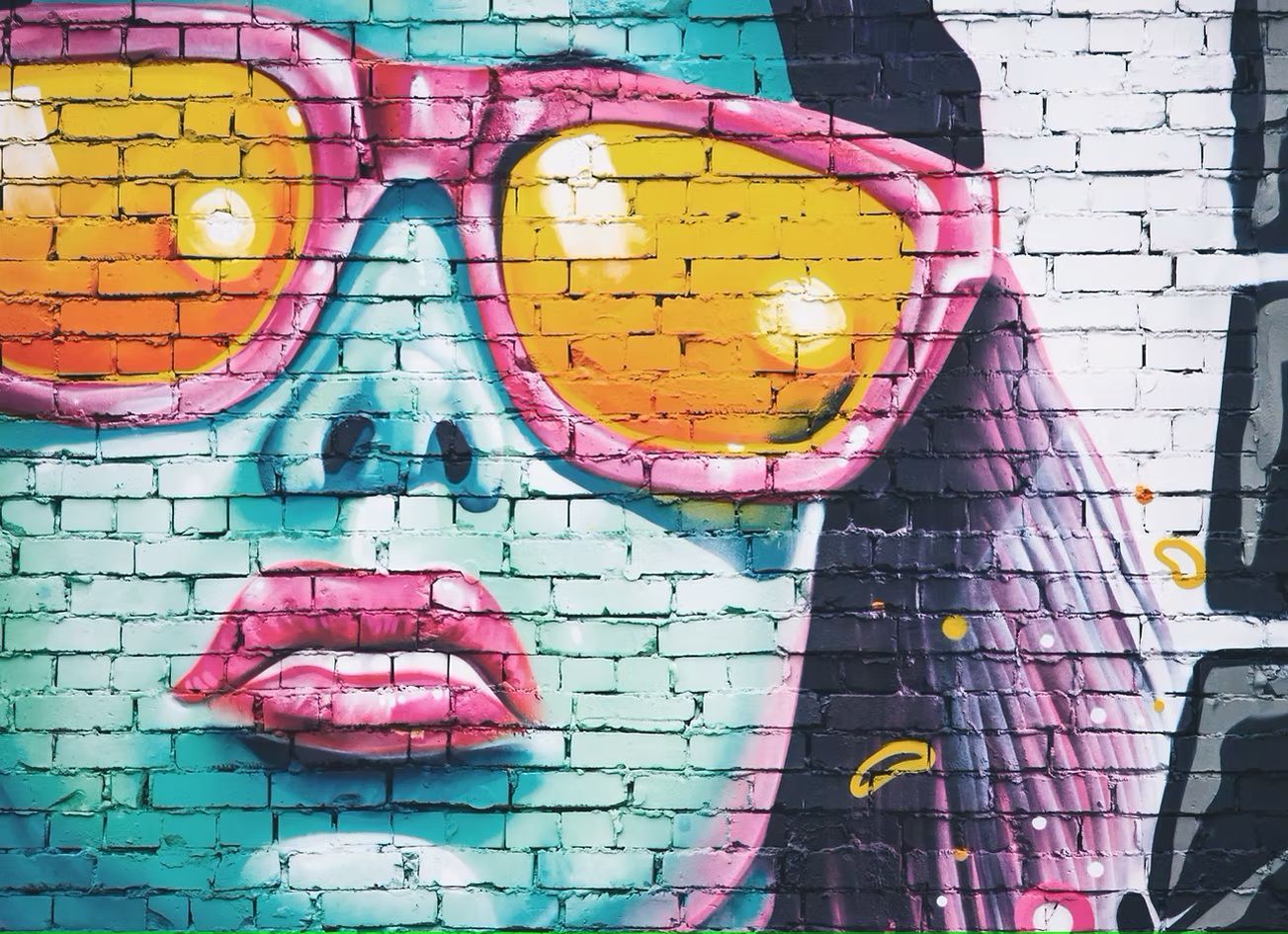 Colorful mural of a face with pink sunglasses and lips on a brick wall