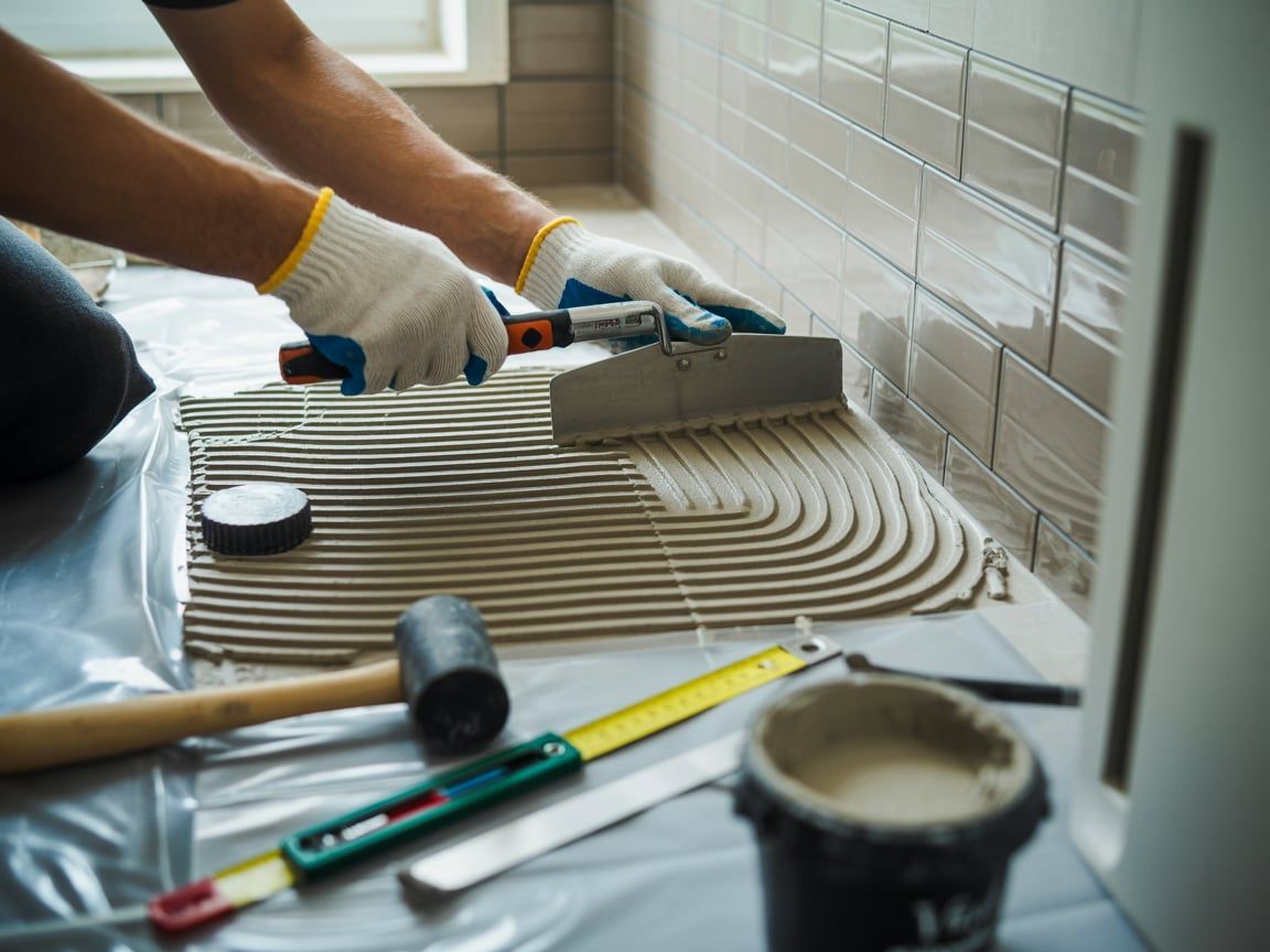 Person tiling a surface with a trowel, surrounded by tools and materials.