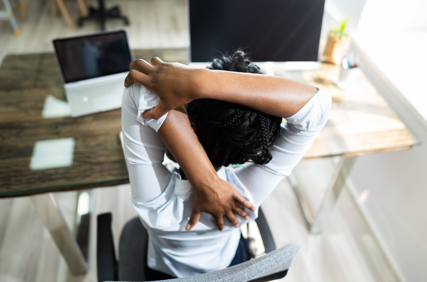 Woman stretching back at her desk with a laptop and monitor in the background.