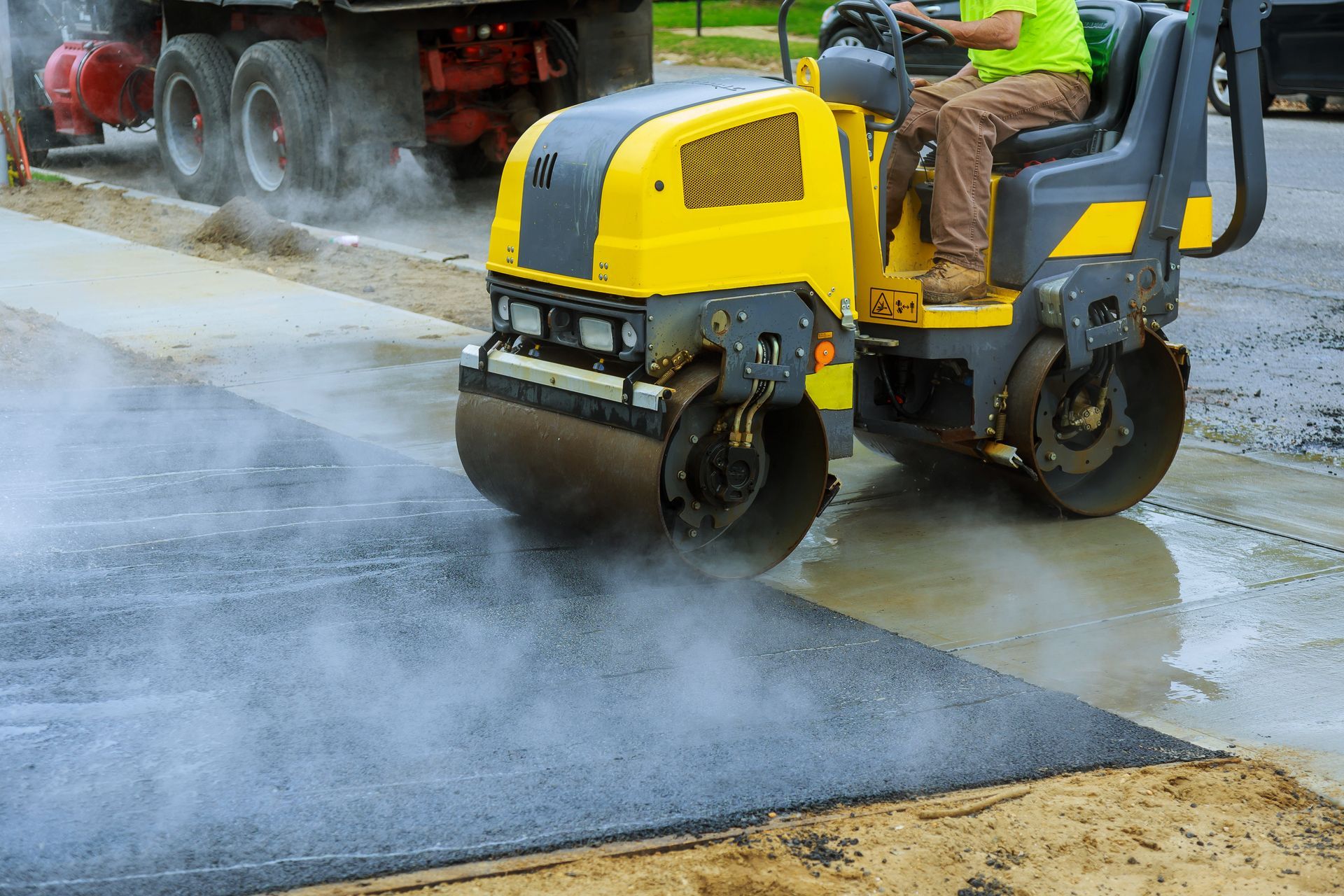 Yellow road roller compacting fresh asphalt, worker driving.