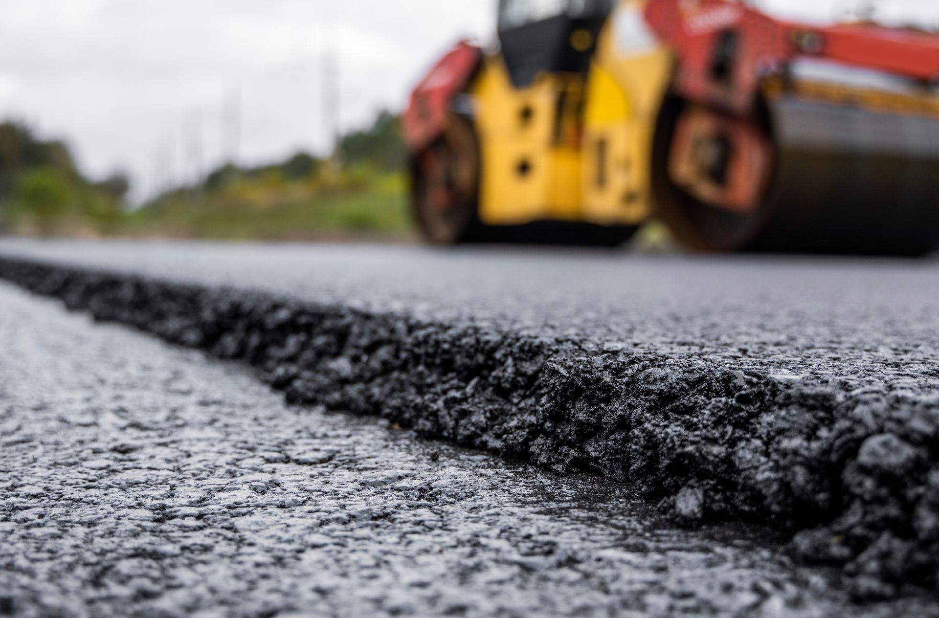 Steamroller compacting asphalt on a road; close-up of fresh black asphalt.
