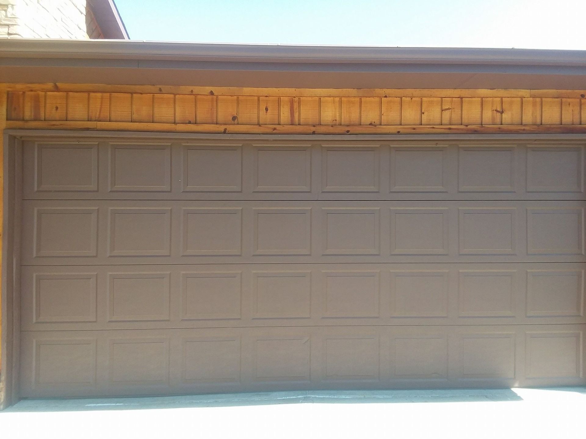 A brown garage door with a wooden roof and gutter on a sunny day.