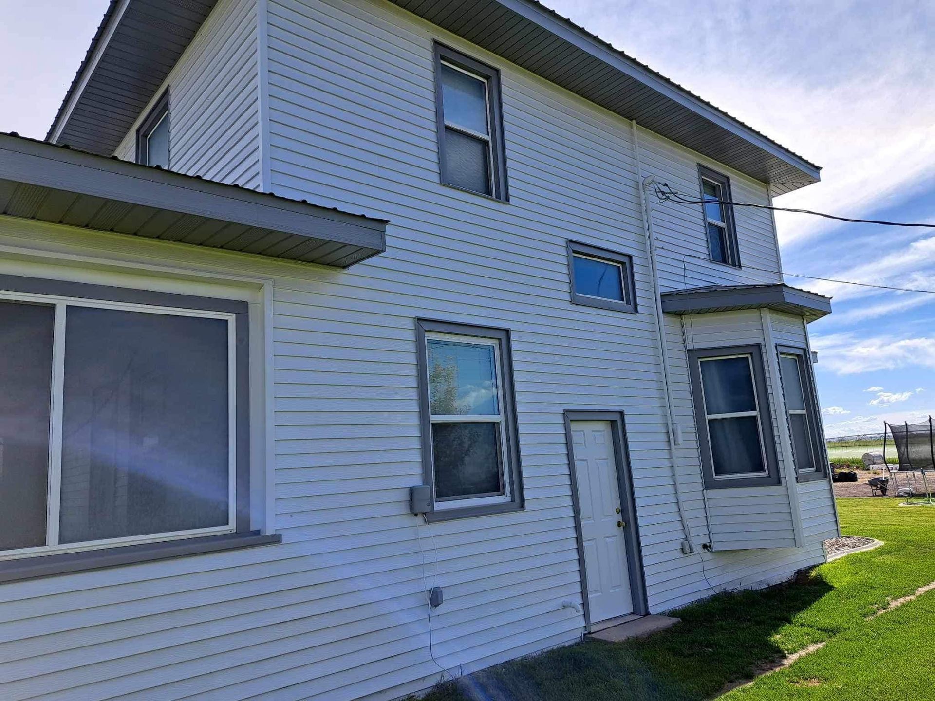A white house with a lot of windows is sitting on top of a lush green field.